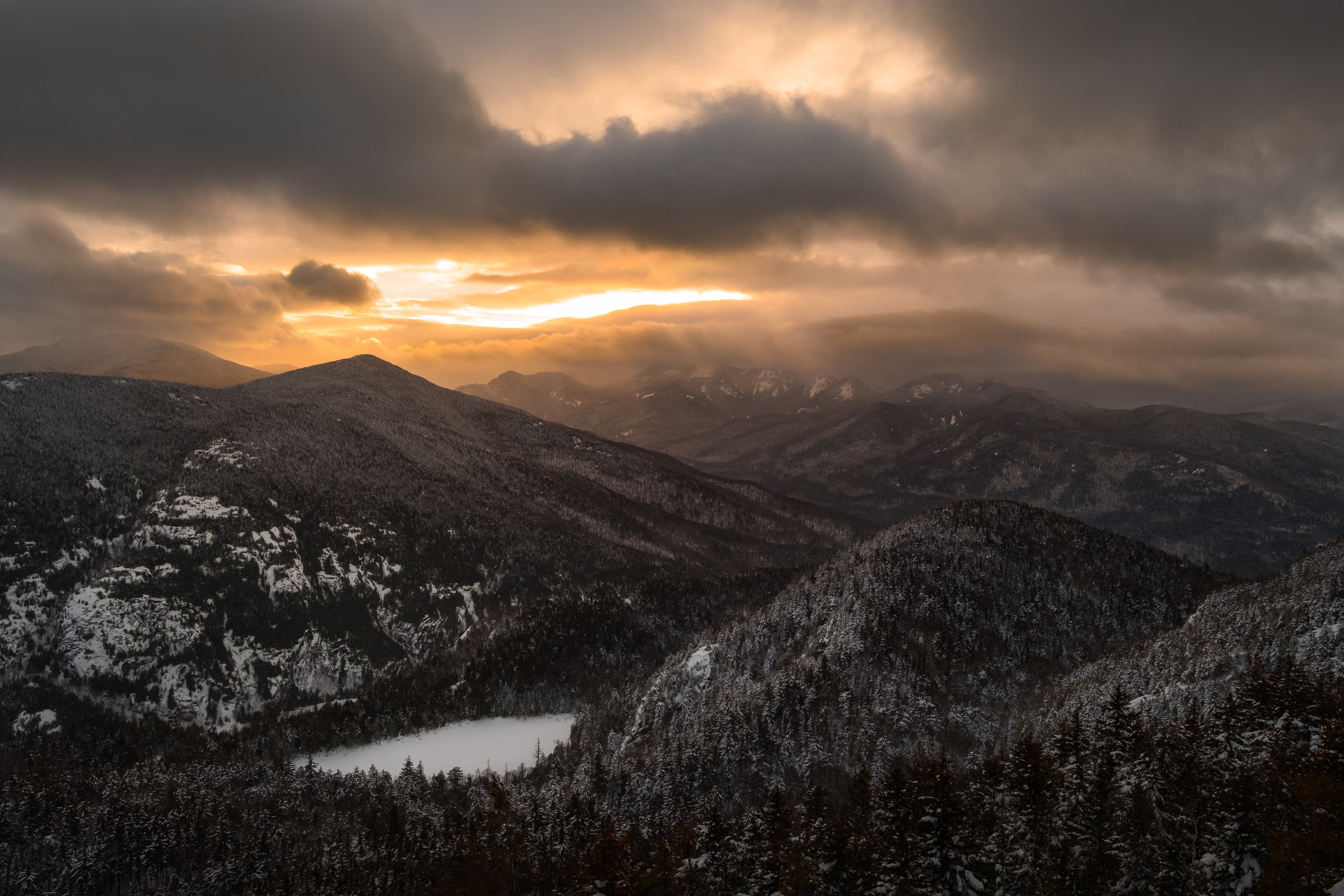 RS76530__DSF7057 Photo of Adirondack Mountains with a cloudy gray sky and sun peaking through.