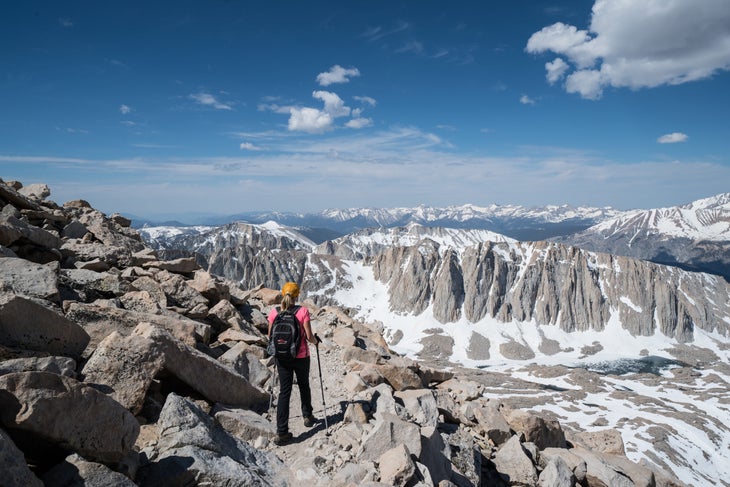 A woman hikes along Trail Crest, on the way down from the summit of Mt. Whitney, overlooking eastern peaks of Sequoia National Park covered in snow.