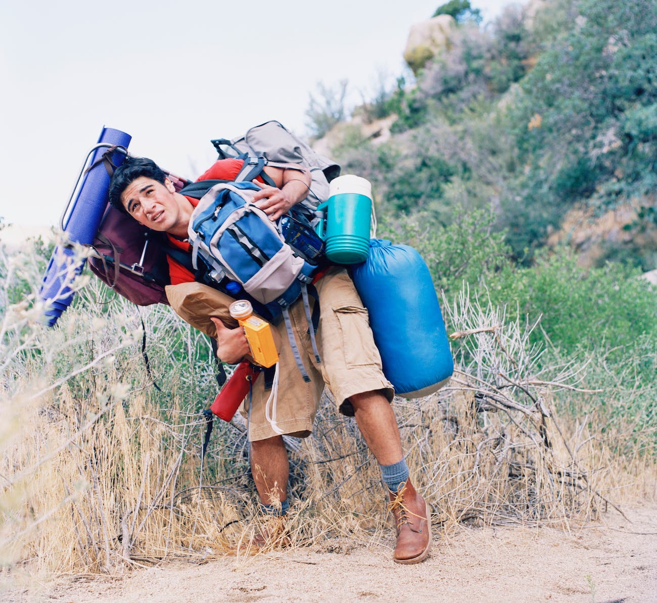 Young man carrying too much backpack and camping gear all on his body.