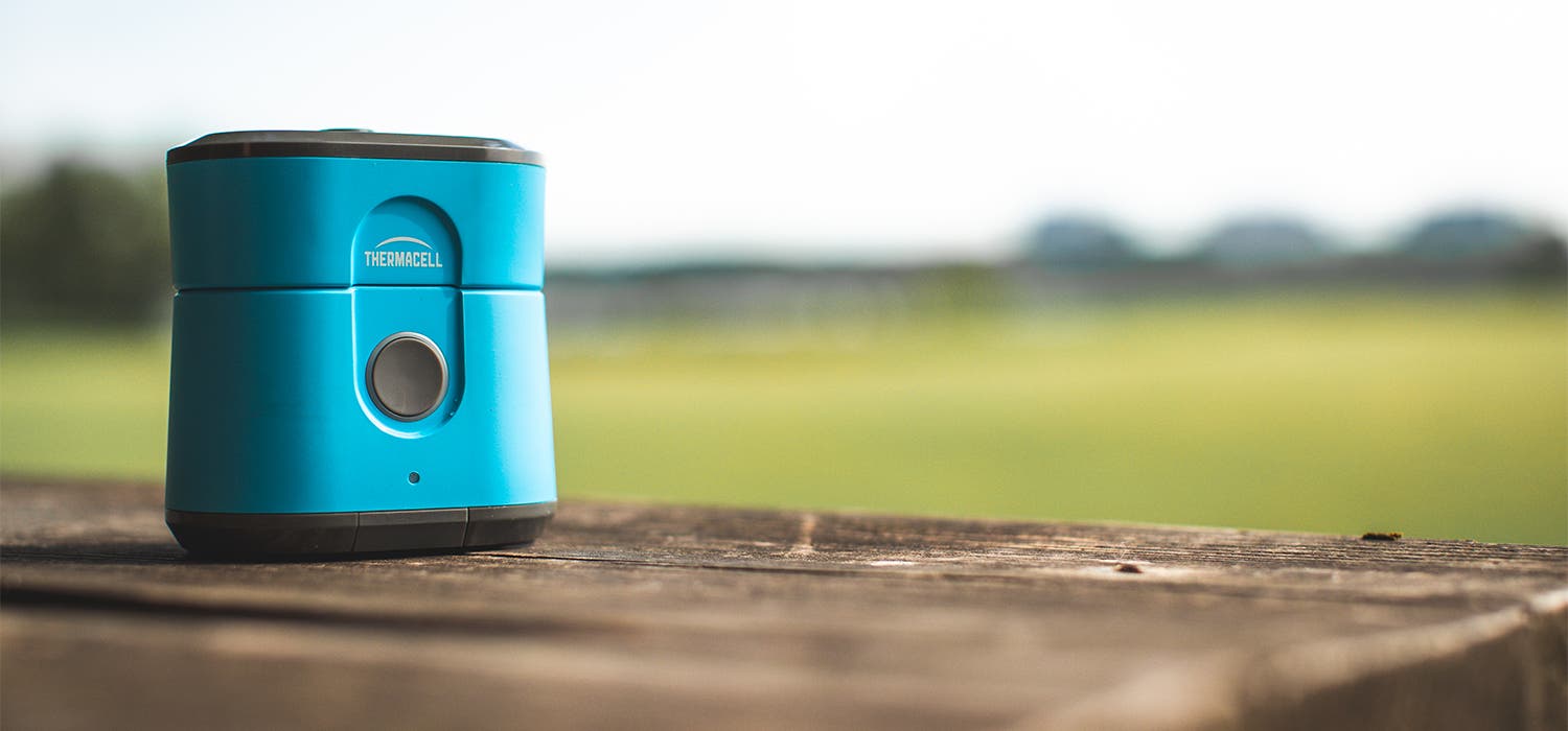 A light blue Thermacell Radius Mosquito Repellant sits on a wooden surface with a green out of focus background.