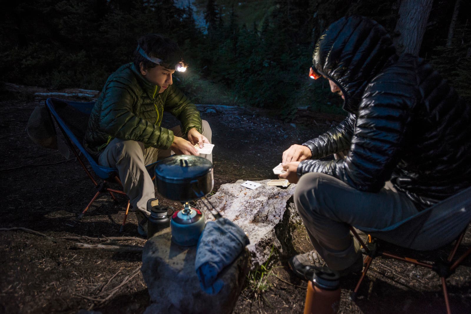 Friends playing card game while camping in forest at dusk