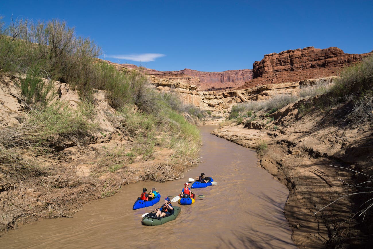 A group of women packrafting on a desert river.