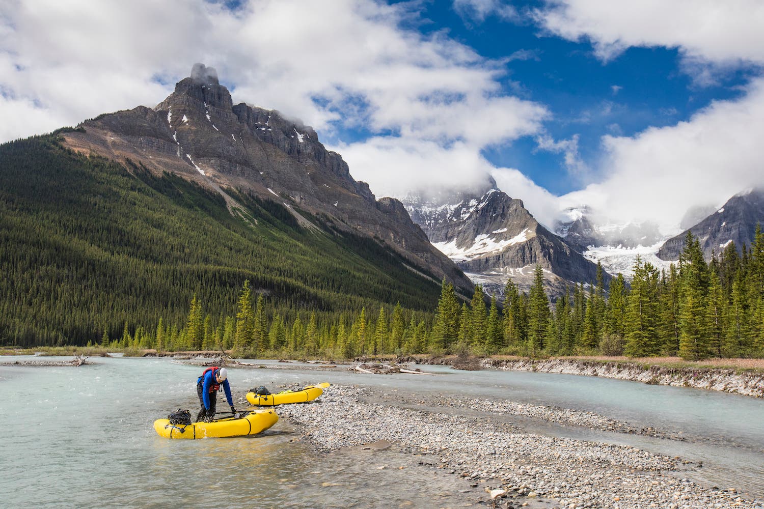 Paddler prepares to launch yellow inflatable raft into scenic river.