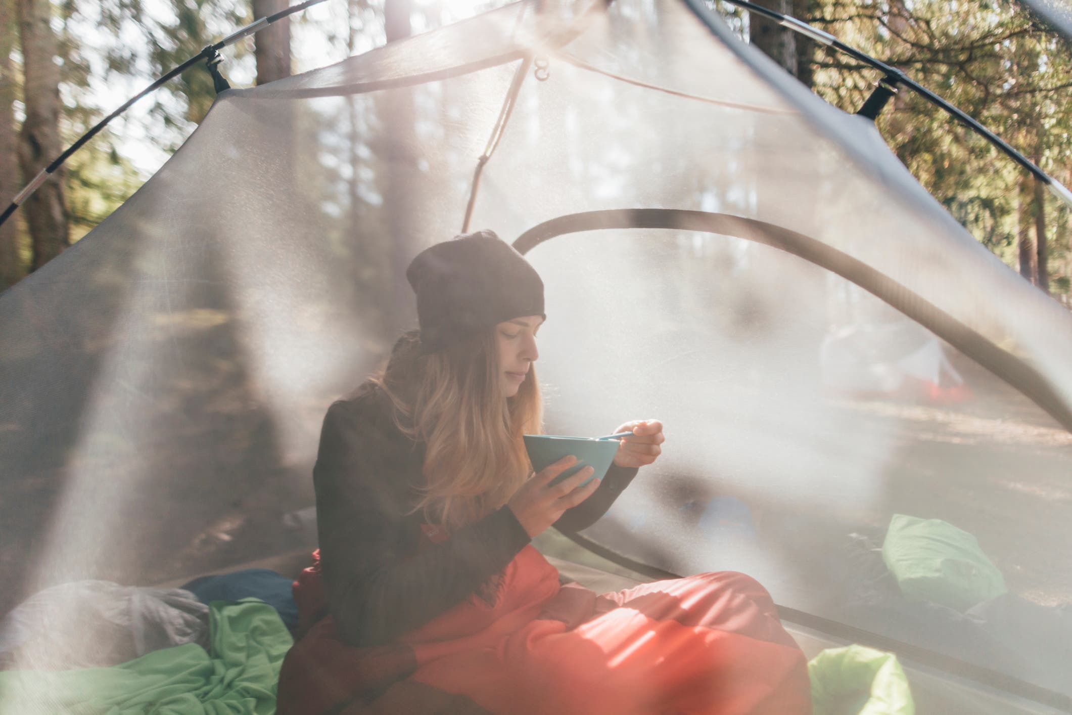 A woman sits in a tent eating from a bowl.