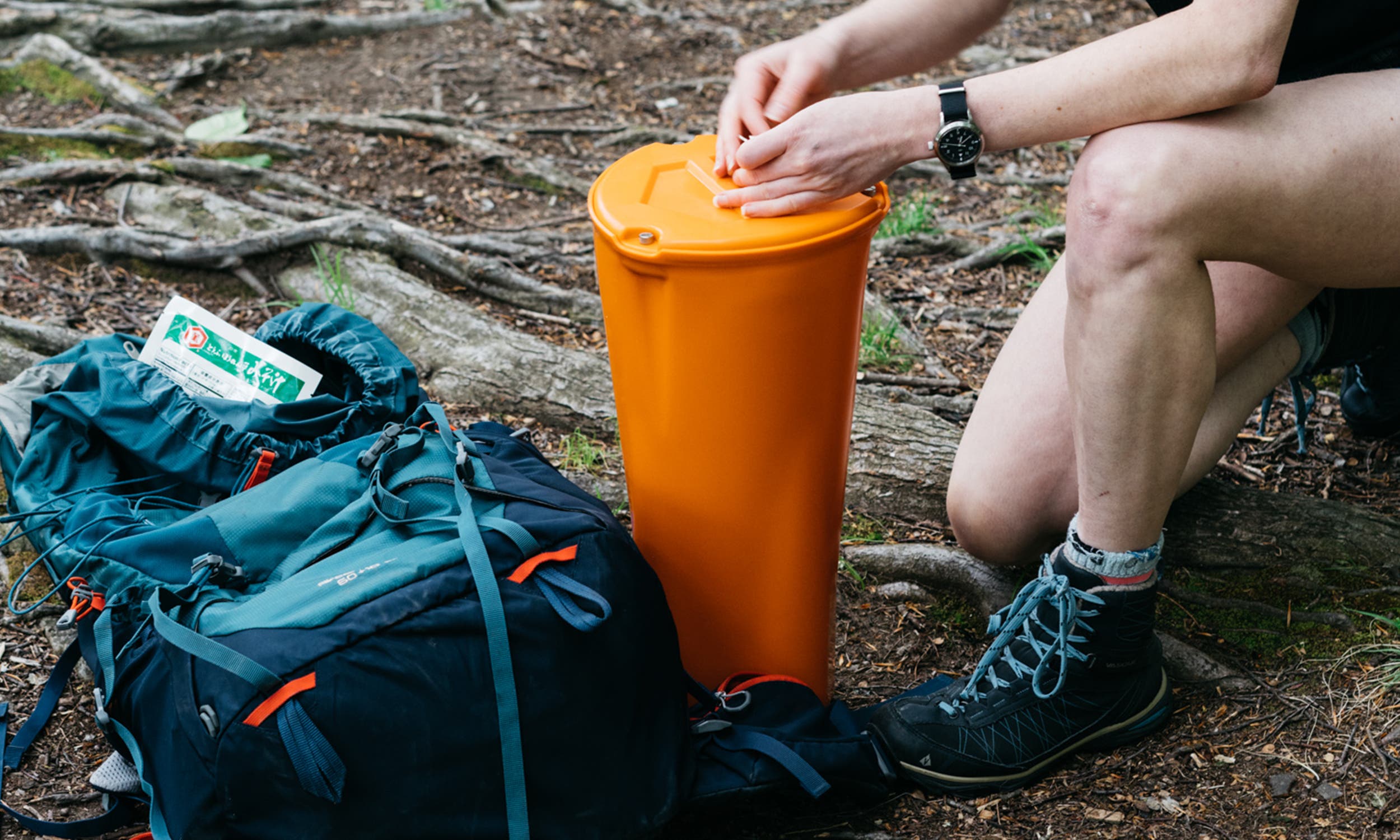 Person opening a bear canister on the ground next to backpack.