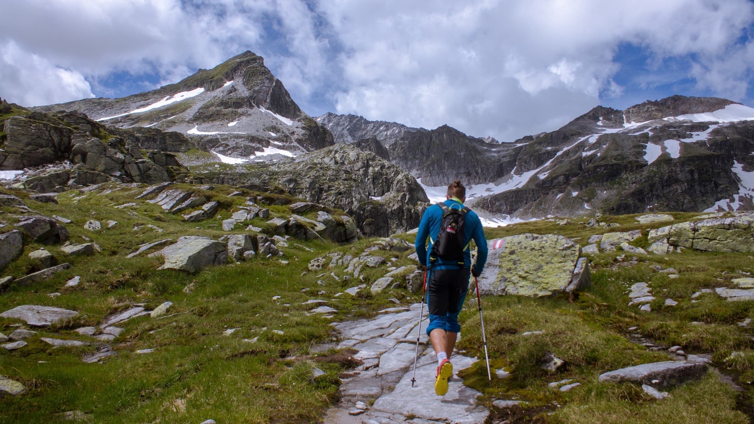 A hiker ascends a trail toward rocky mountains.