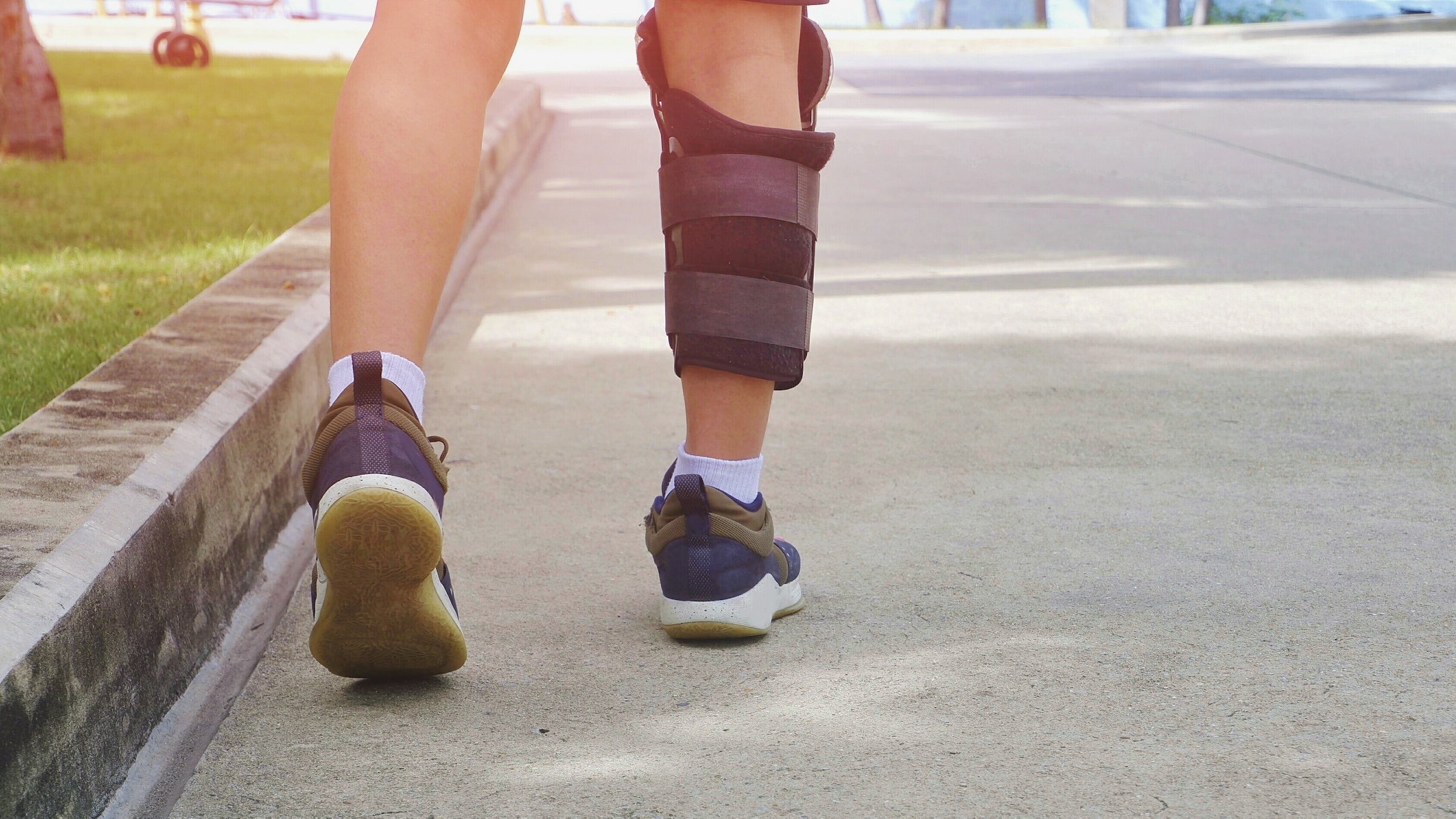 Low section and rear view of young man's legs in supportive knee brace is jogging on concrete floor at public park in morning time
