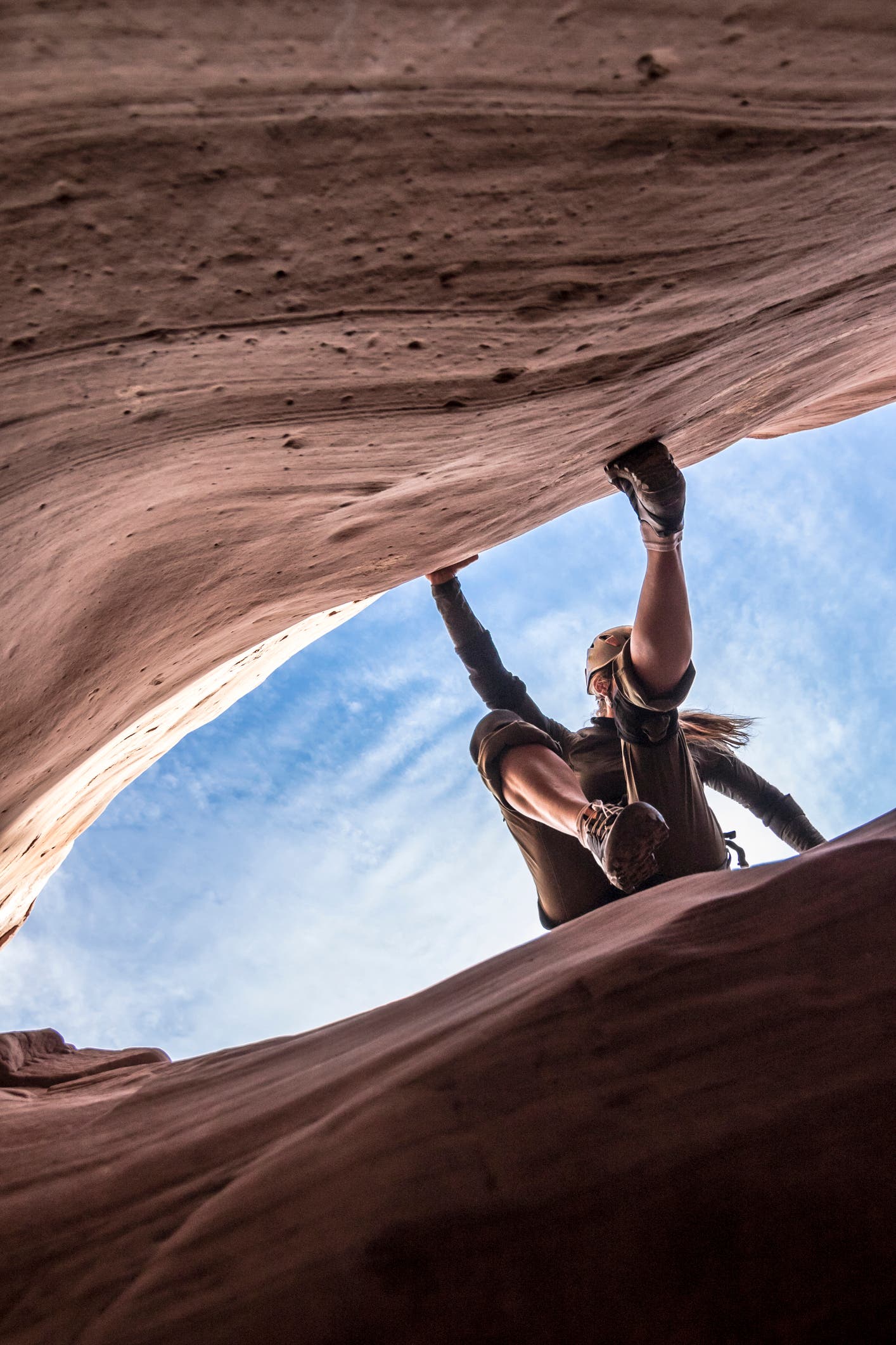 Female canyoneer with hands and feet pressed against sandstone walls, the blue sky behind her.
