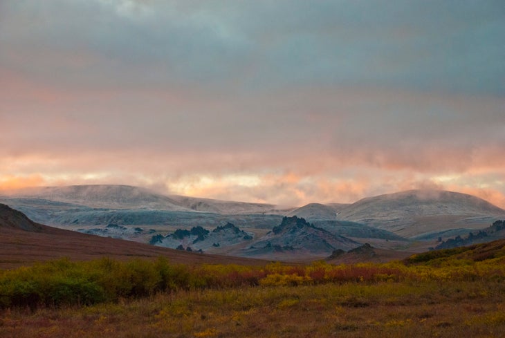 red and yellow tundra in front of low mountains with light snow over the summits