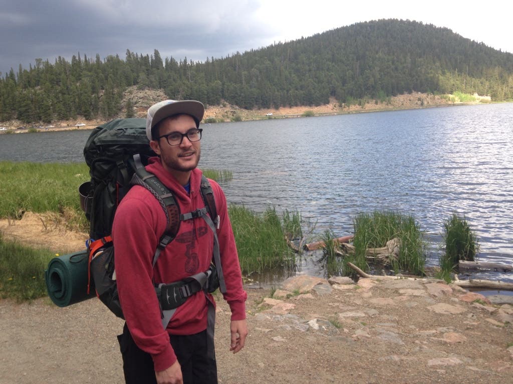 A backpacker smiles in front of a lake