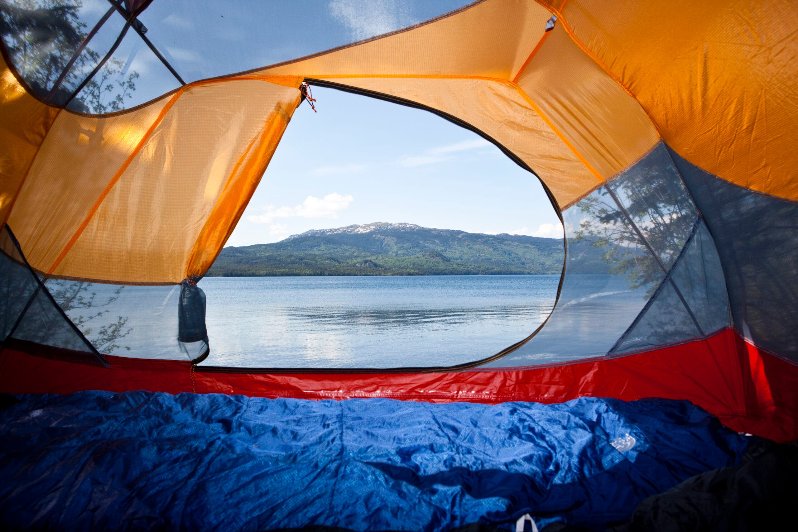 from inside a tent with a sleeping bag inside, with a lake and distant mountains visible in the background