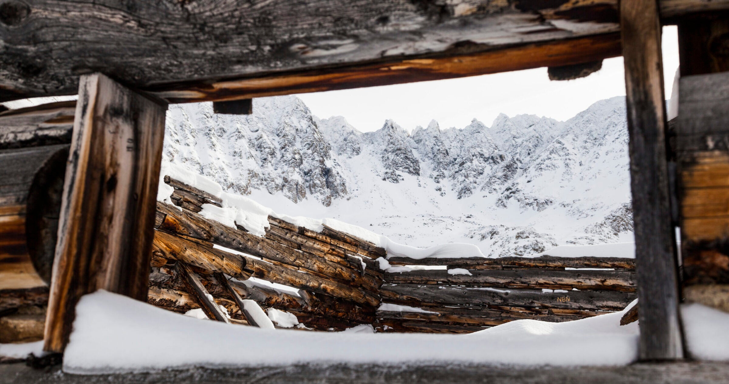 Jagged mountain peaks seen through the window of a ruined log cabin at Boston Mine in Mayflower Gulch, Tenmile Range, Colorado.