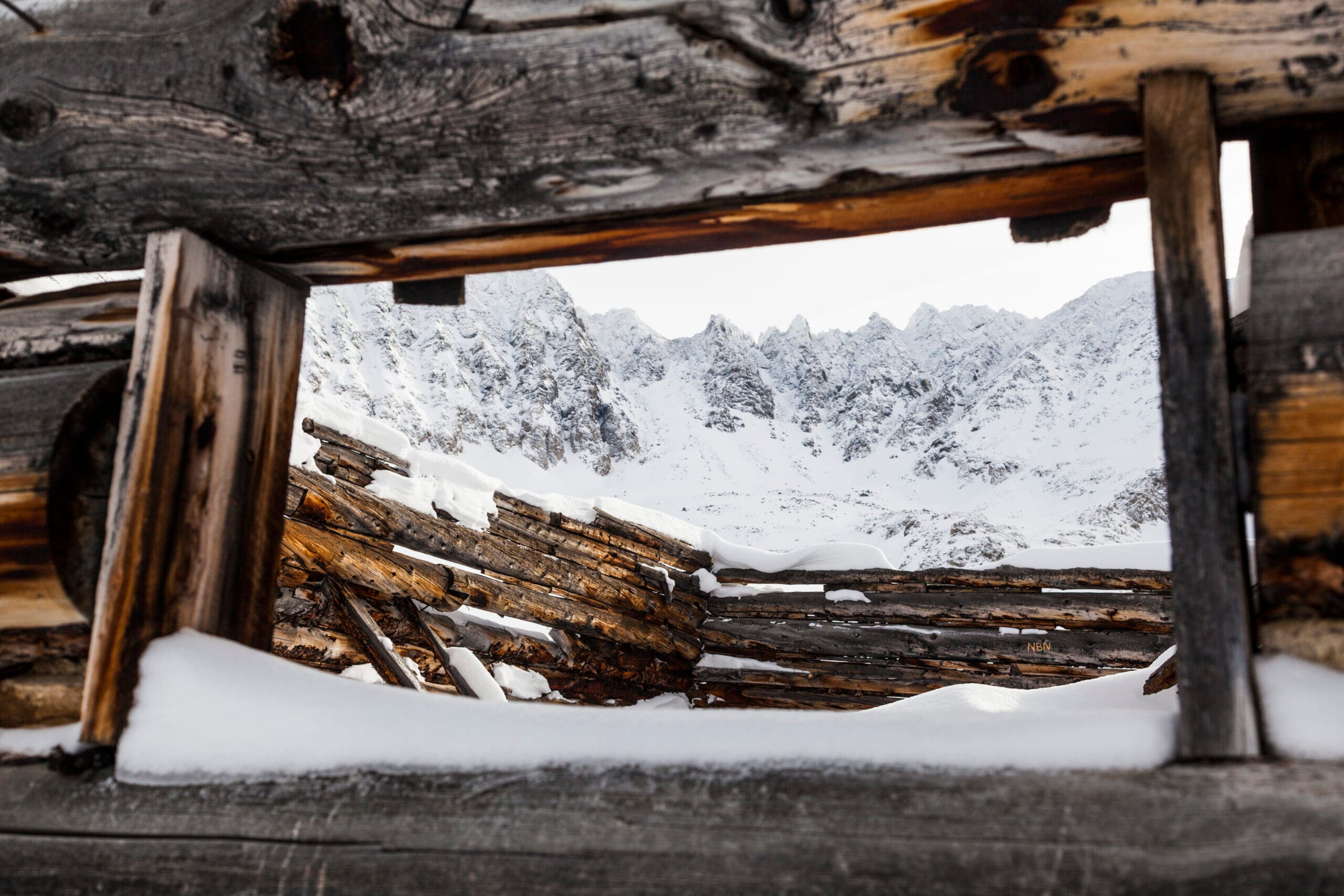 Jagged mountain peaks seen through the window of a ruined log cabin at Boston Mine in Mayflower Gulch, Tenmile Range, Colorado.