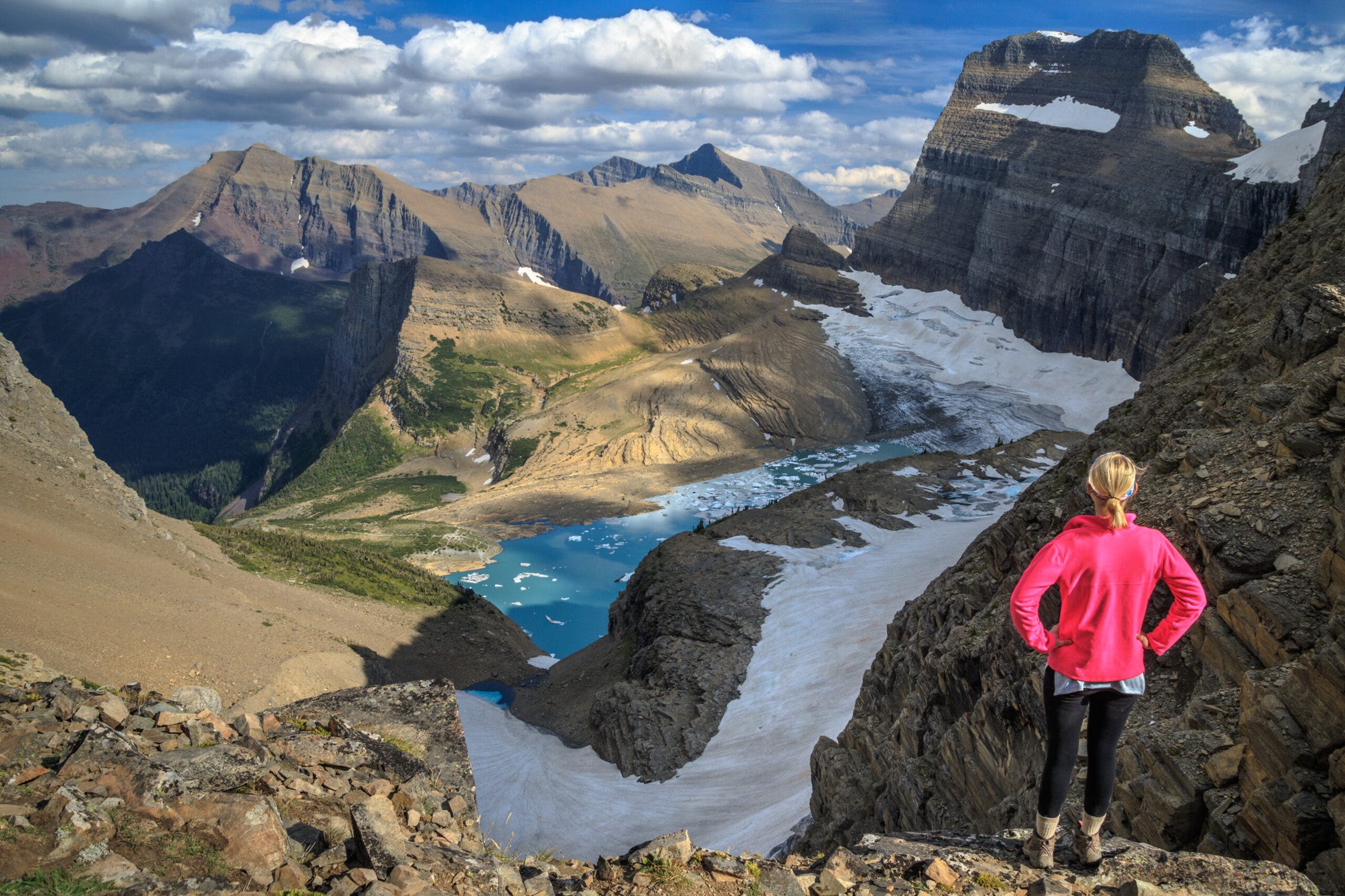 a female hiker on a ridge looks down at Grinell Glacier and Grinell lake in Glacier National Park