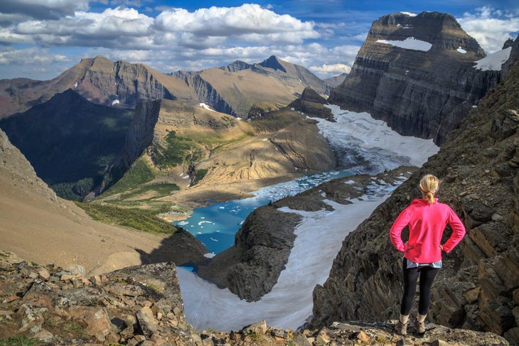 a female hiker on a ridge looks down at Grinell Glacier and Grinell lake in Glacier National Park