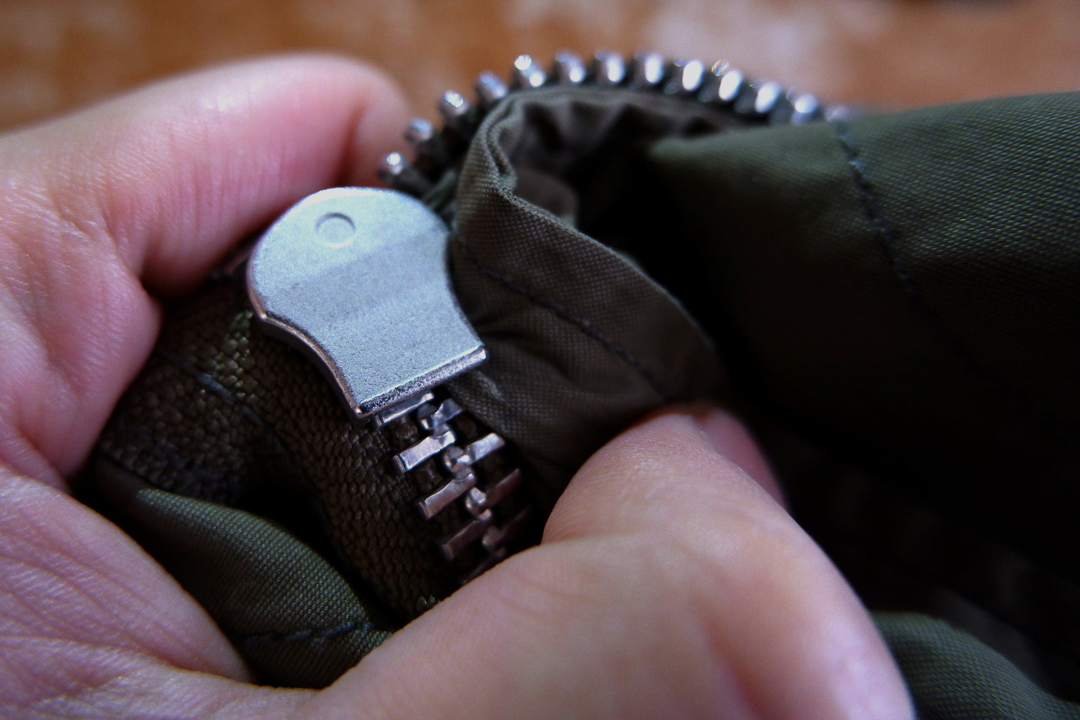 A close up of stuck zipper on a dark green jacket, holding by a hand