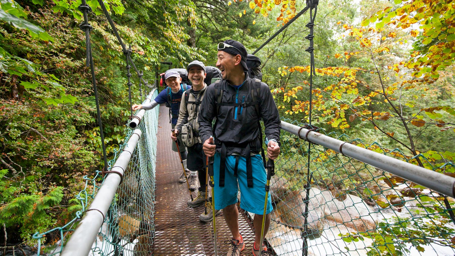 hikers use trekking poles while crossing a bridge