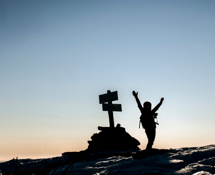 a hiker silhouetted on a summit with arms up in victory