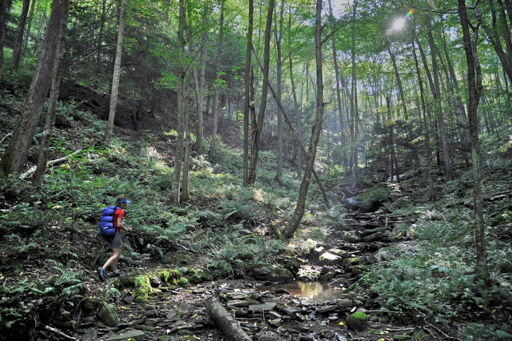 backpacker crossing a forest creek