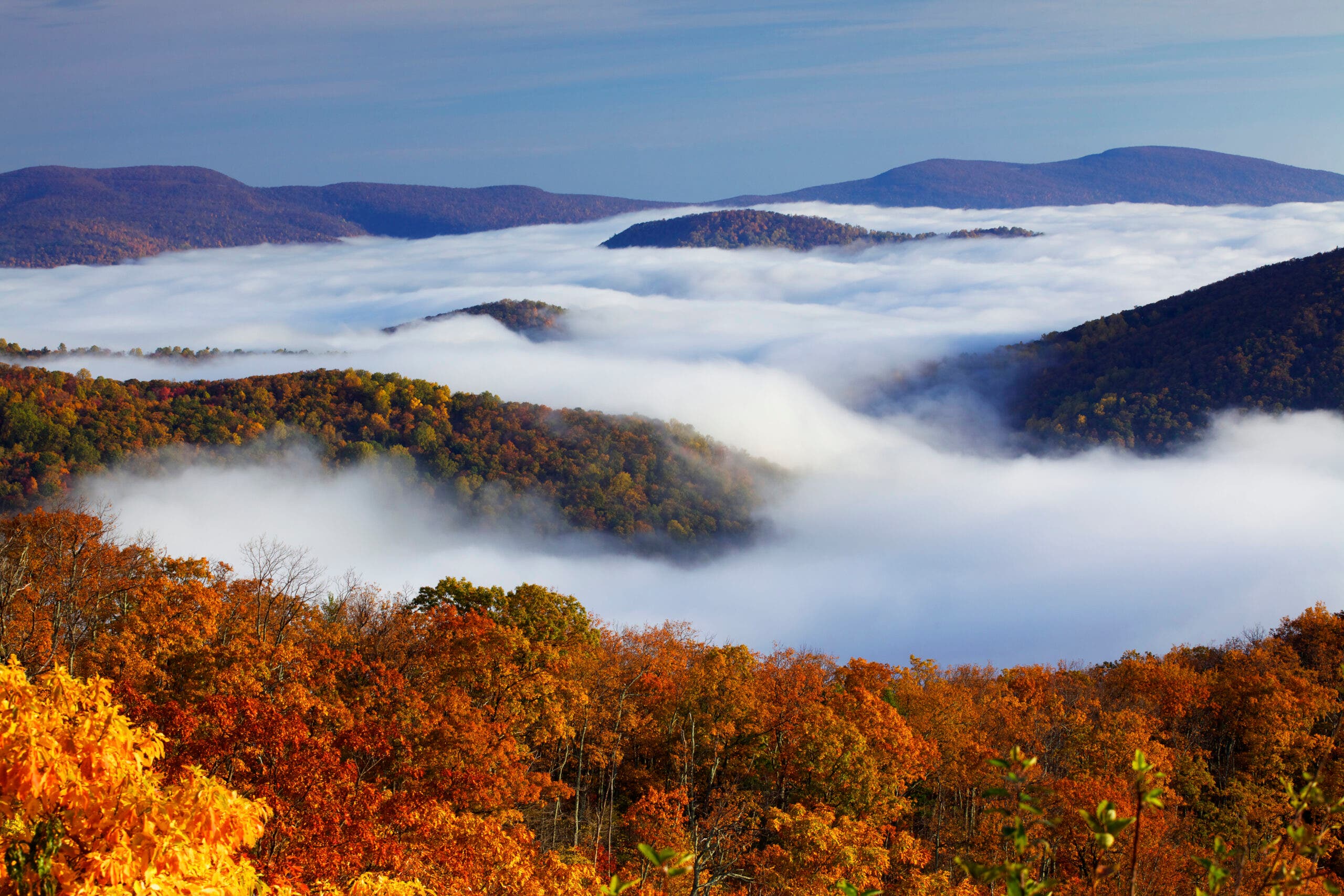 clouds coming in to valleys between forested ridgelines with bright red and orange fall colors