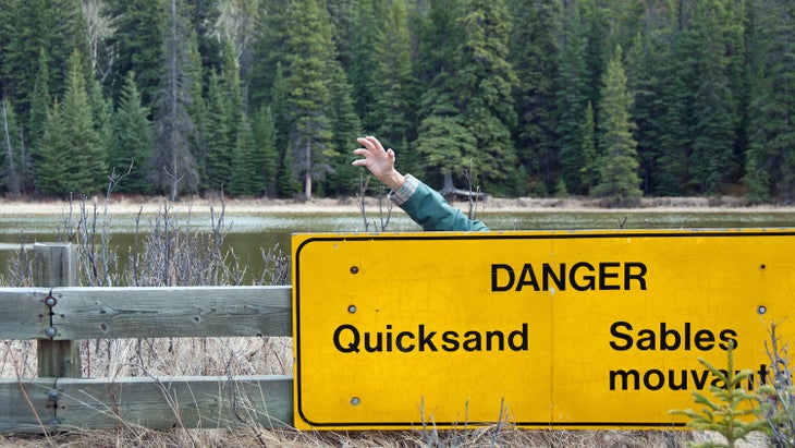 man sinking in quicksand behind sign