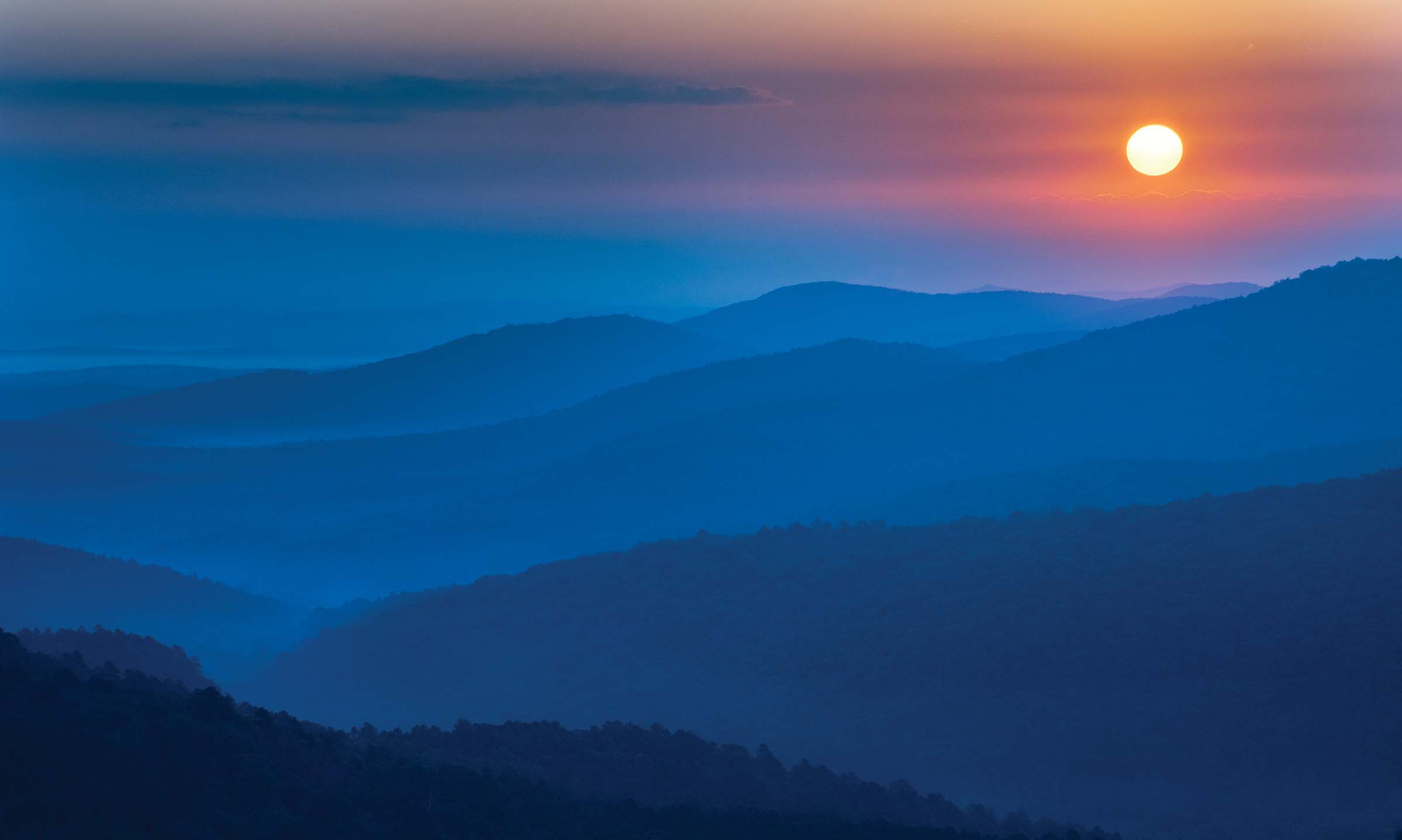 A bright orange sun rises above the dark Ouachita Mountains lighting the way for an early morning start on the Ouachita Trail. 