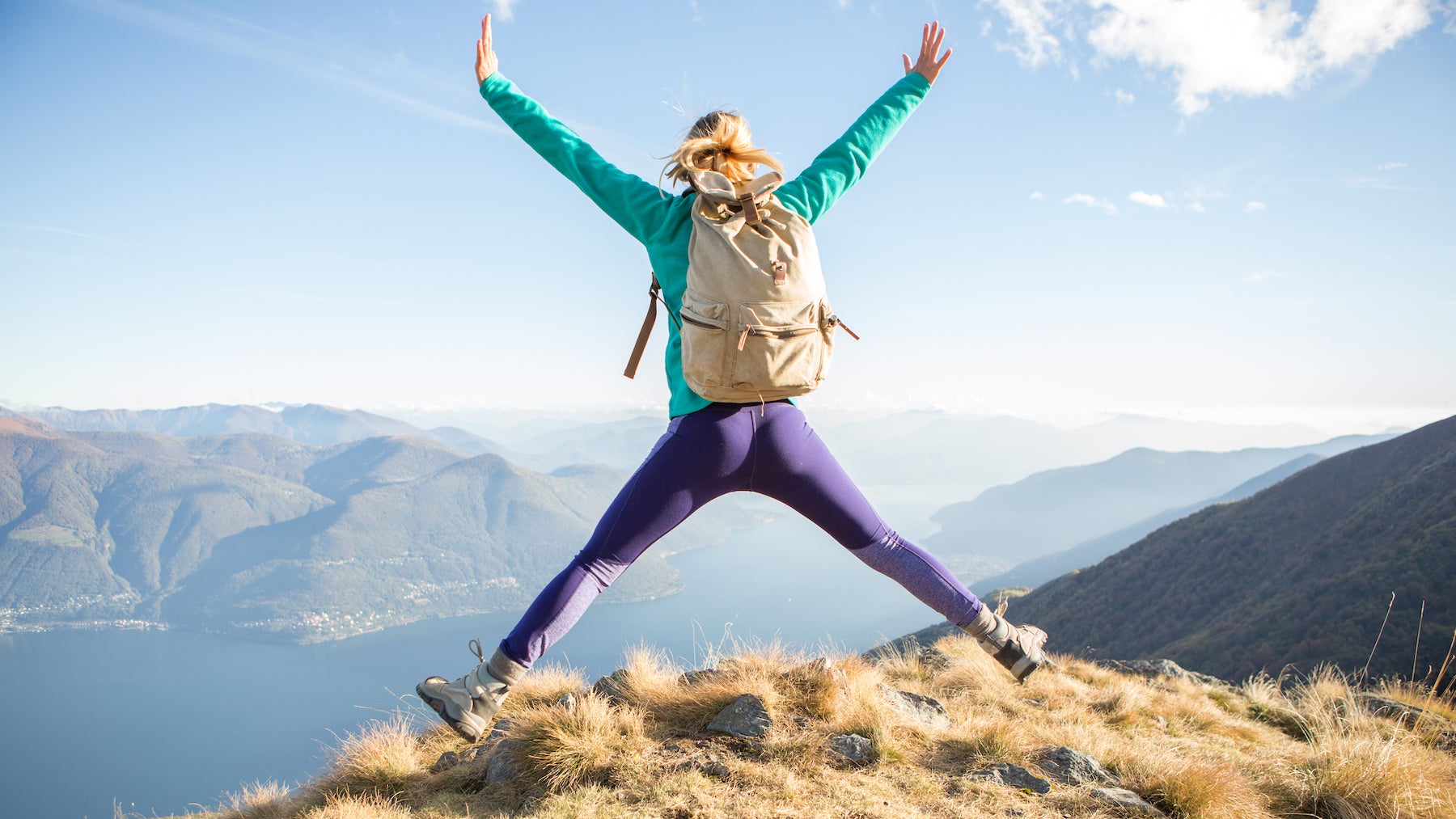 Young hiking woman at the top of a mountain jumping high up.