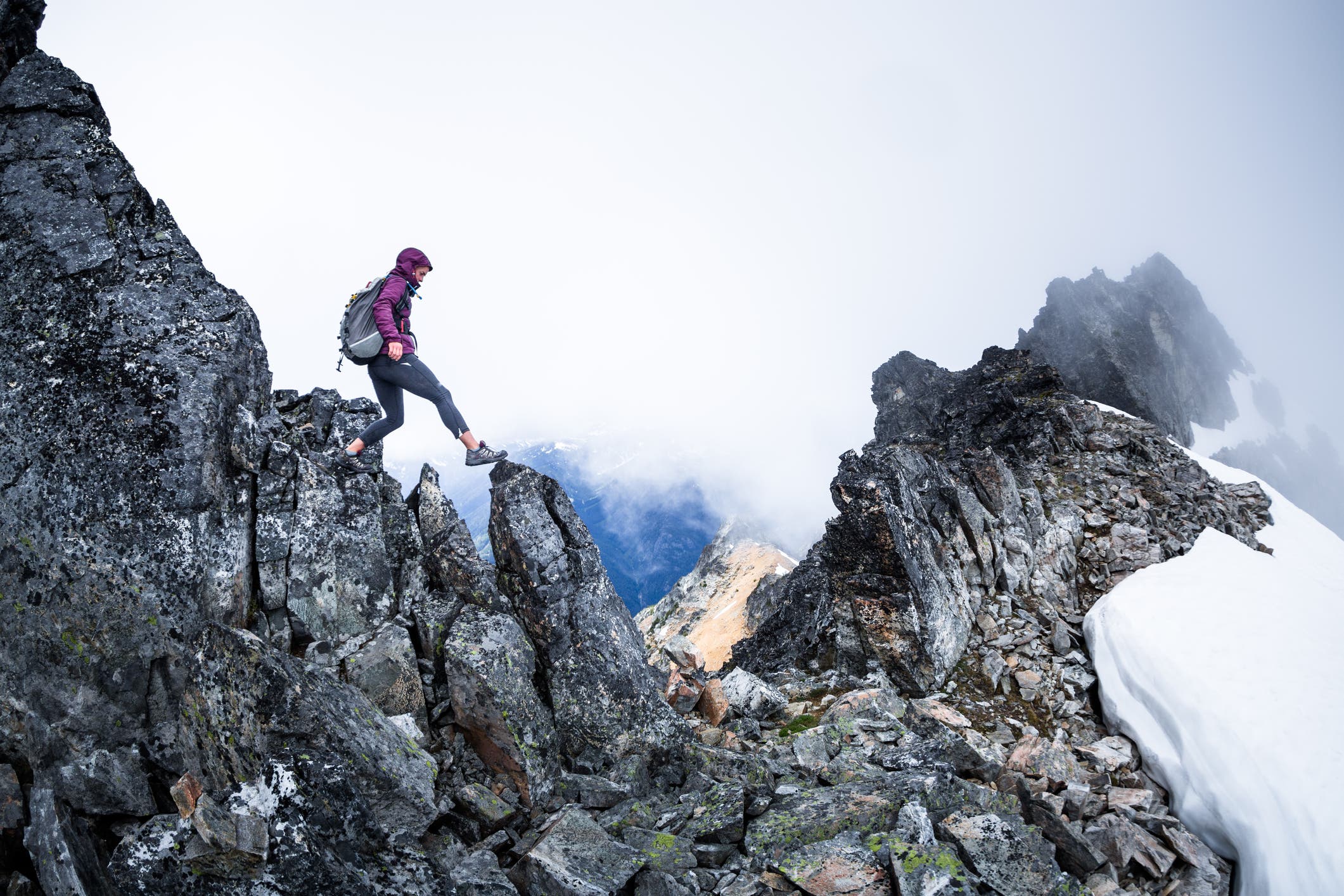 Woman hiking on a narrow ridge surrounded by clouds.