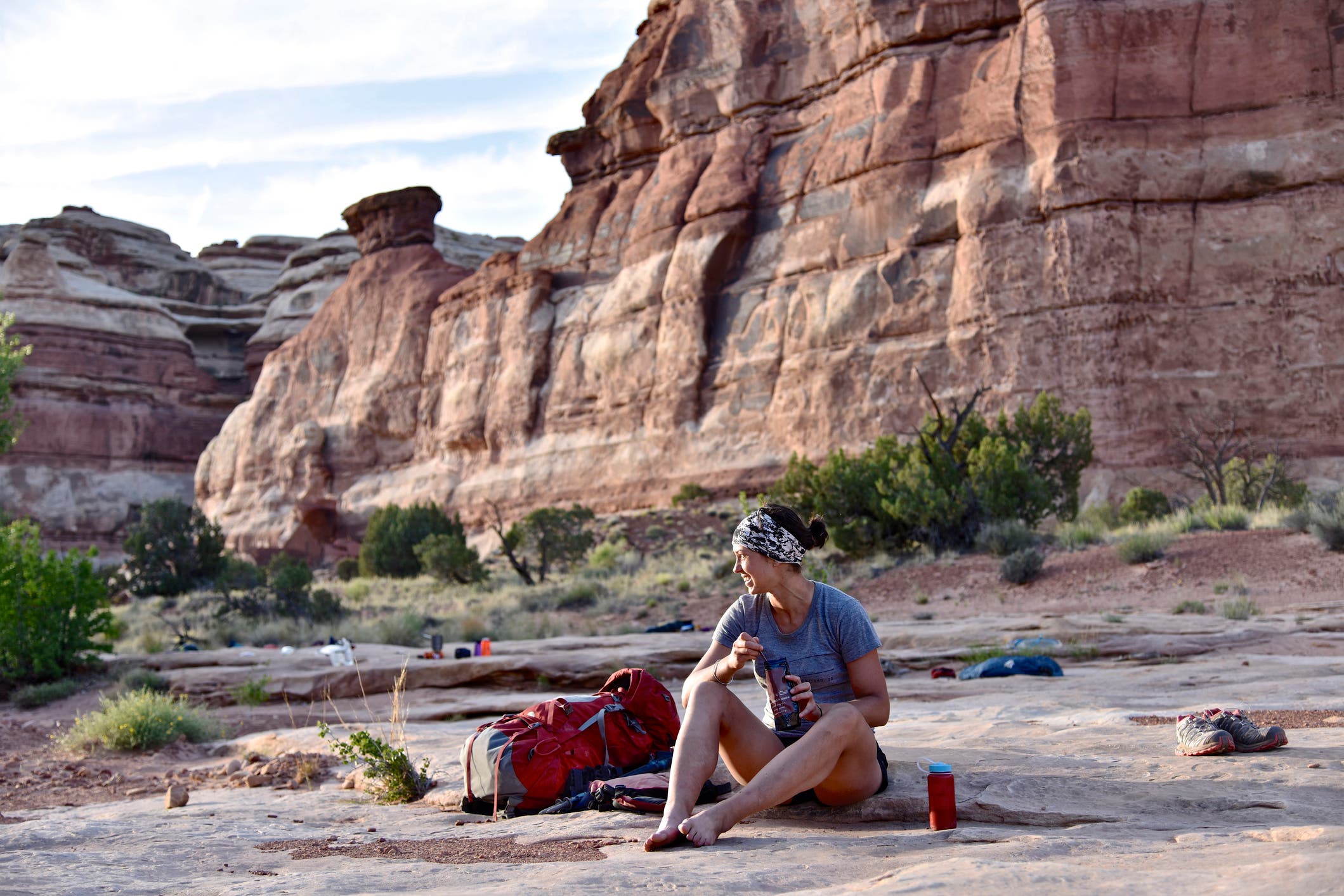 A female hiker sits on the ground eating.
