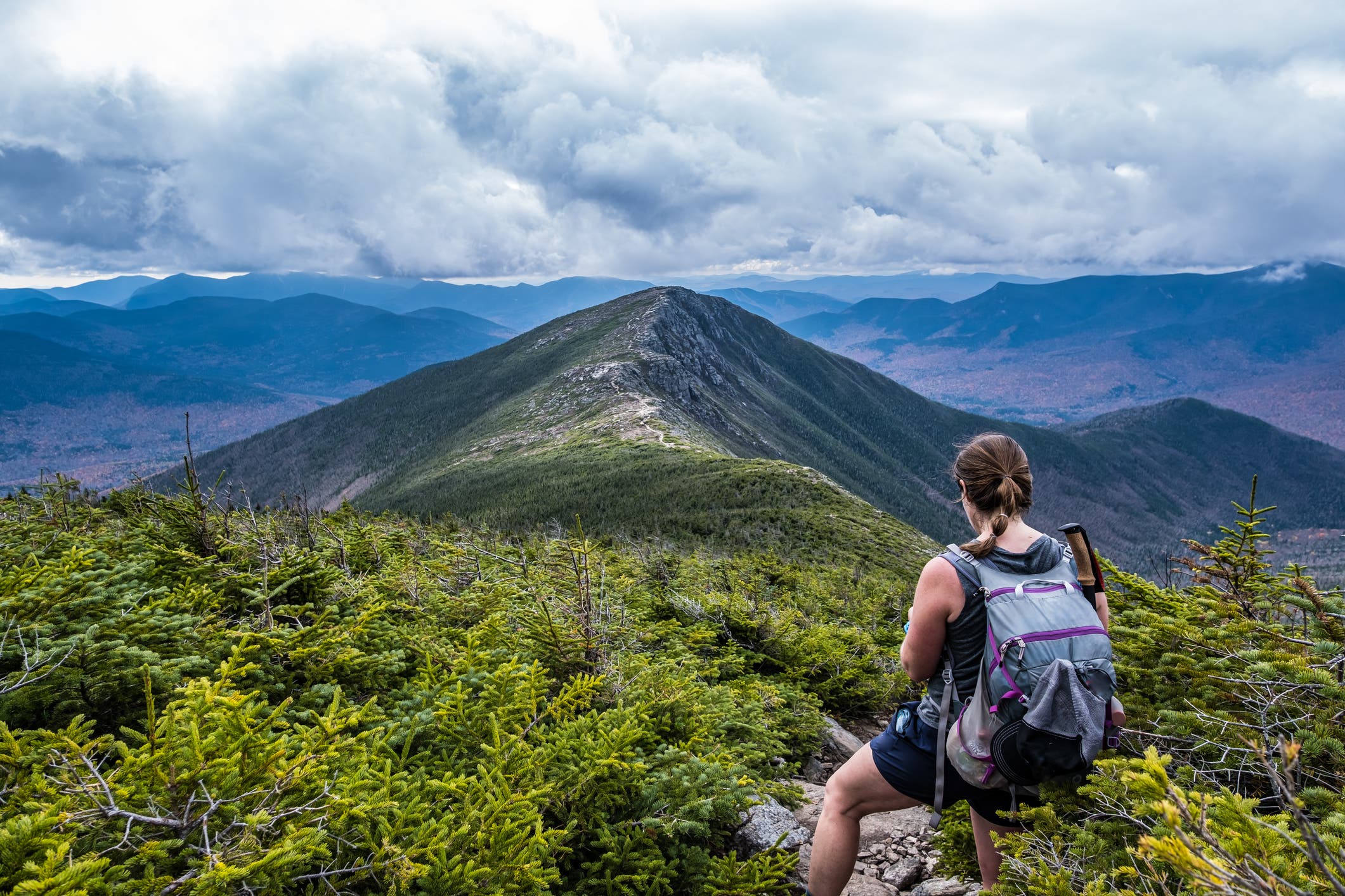 A hiker looks down at a map. A green, rocky ridgeline stretches before her.