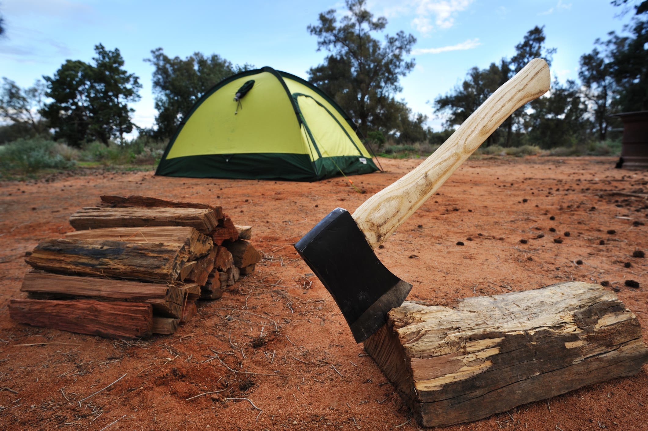 A hatchet lodged in a piece of firewood in front of a tent.