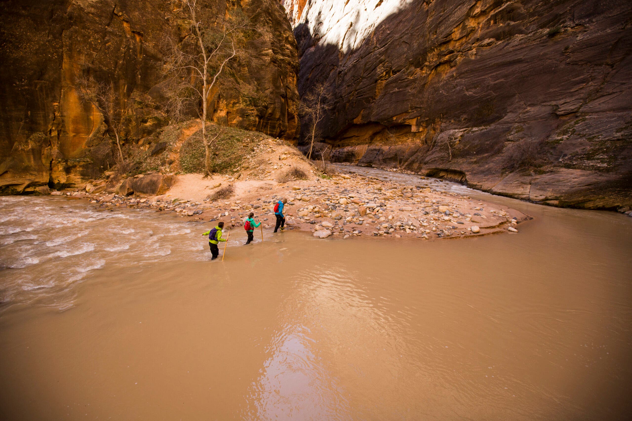 Three hikers crossing a river in Zion National Park