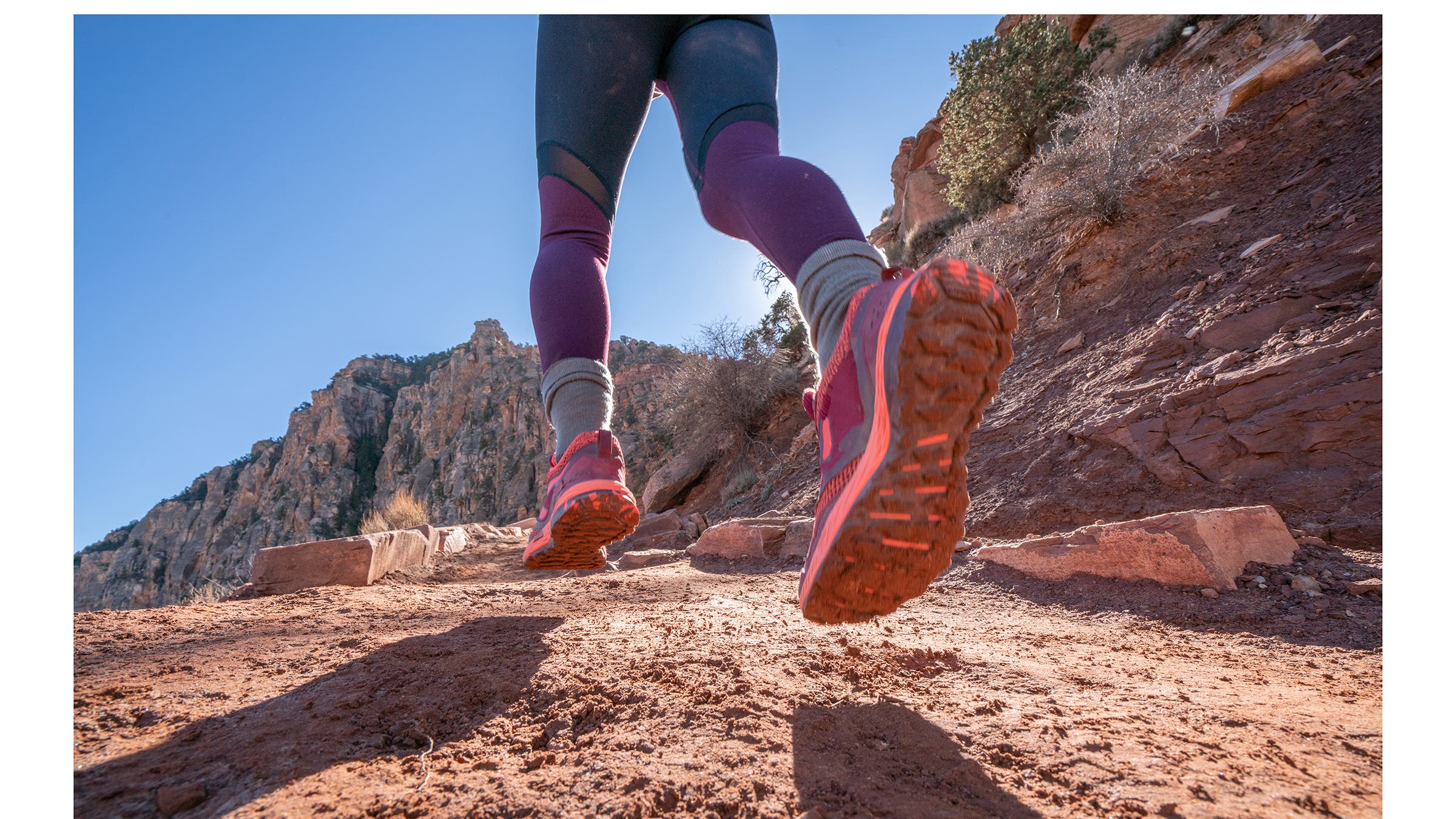 A woman trail running in dusty mountain in the desert.