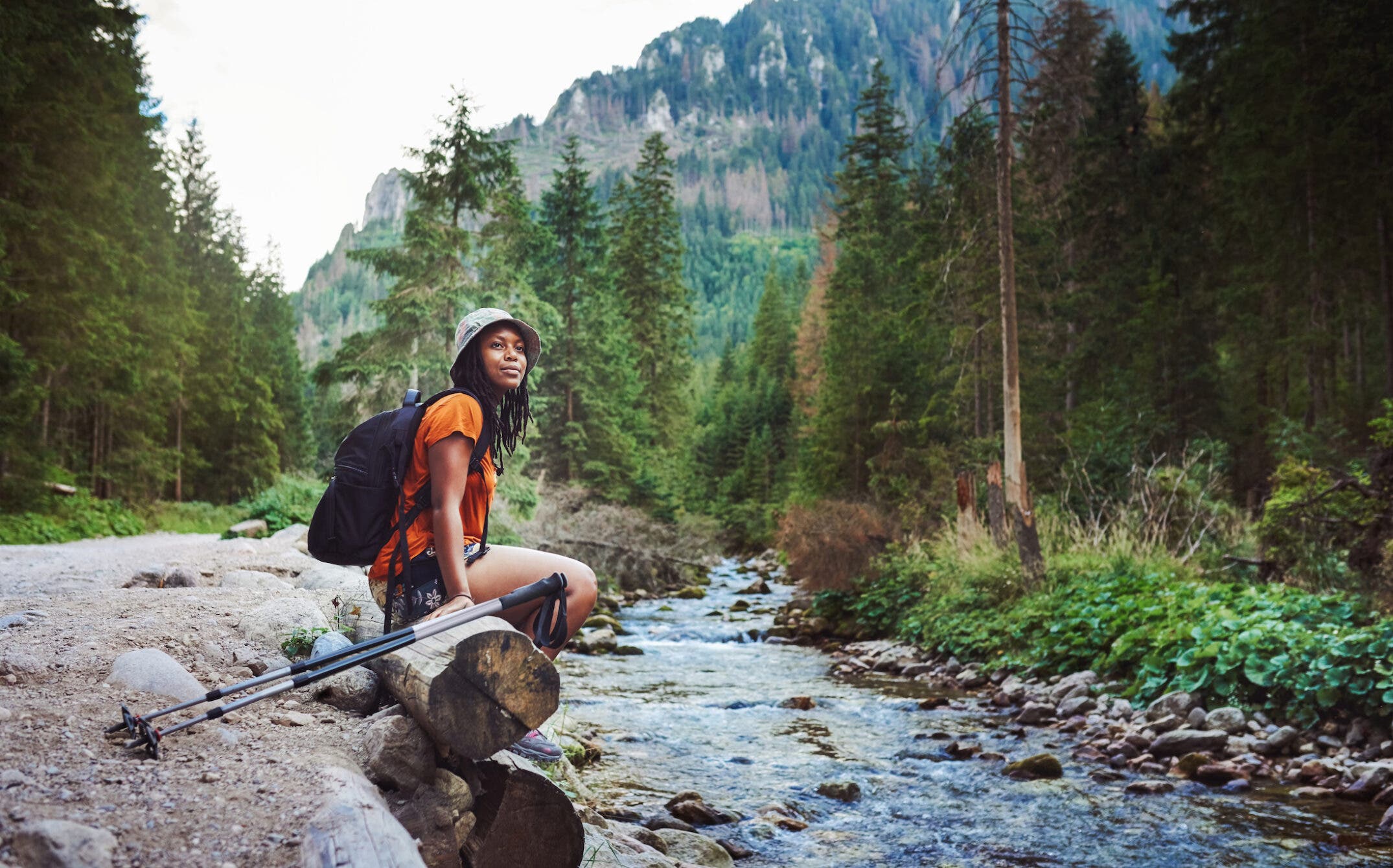 female hiker sitting next to river, with her trekking poles at her side