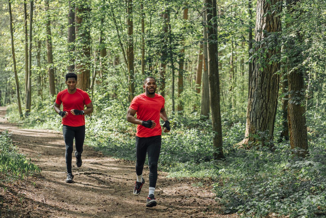 two men running on trail surrounded by trees