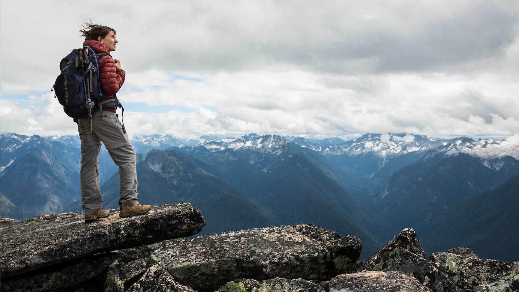 A woman looks out at the North Cascade mountains after hiking to the summit.