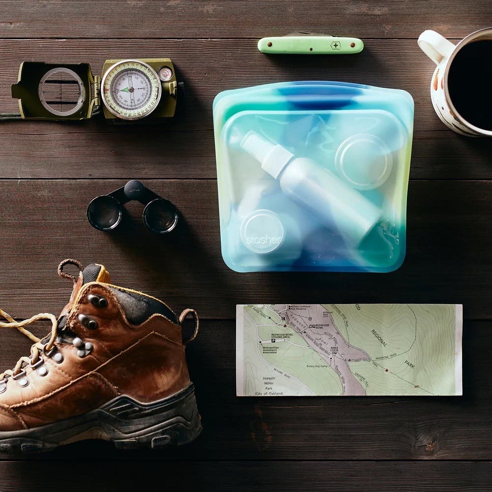 Stasher reusable bags with hiking gear on wooden table