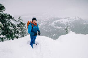 A man wearing outdoor clothing stands in snow on edge of a cliff during a snowstorm