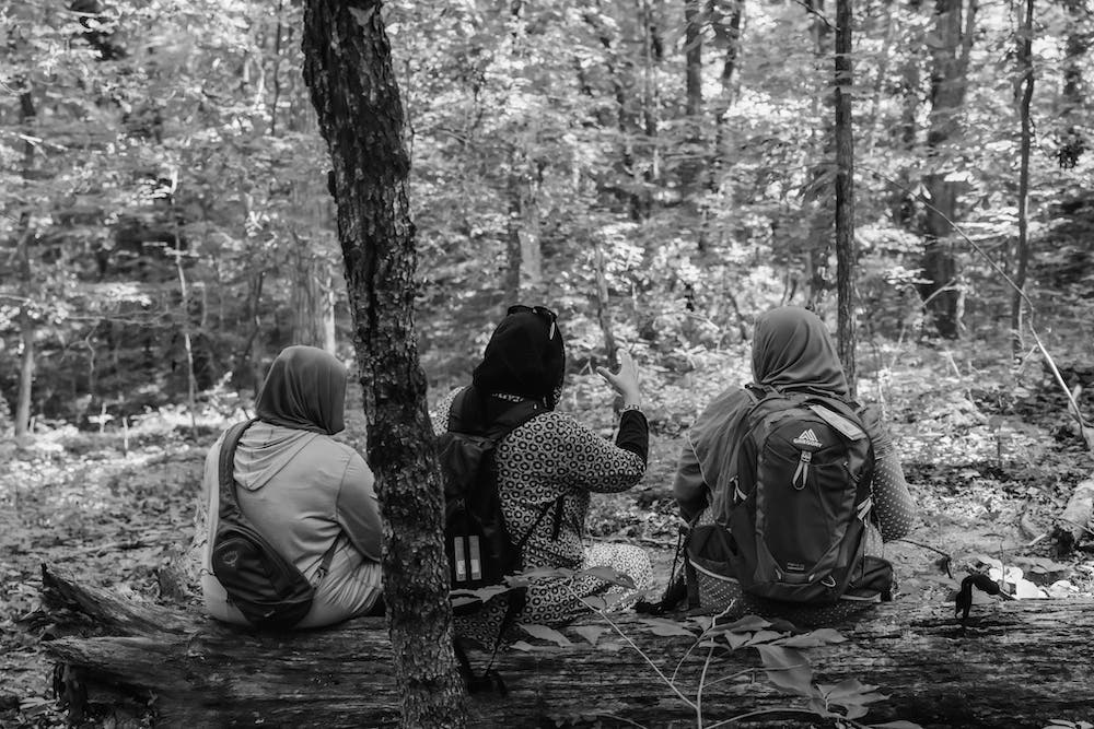 three women sitting under tree on trail