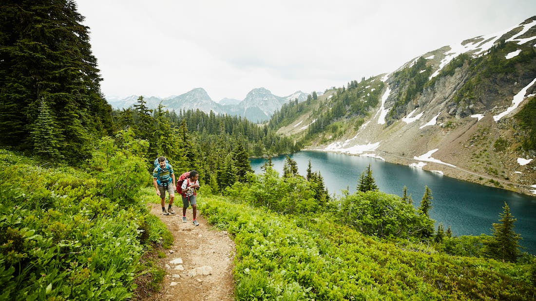 Father and son hiking on mountain trail above alpine lake