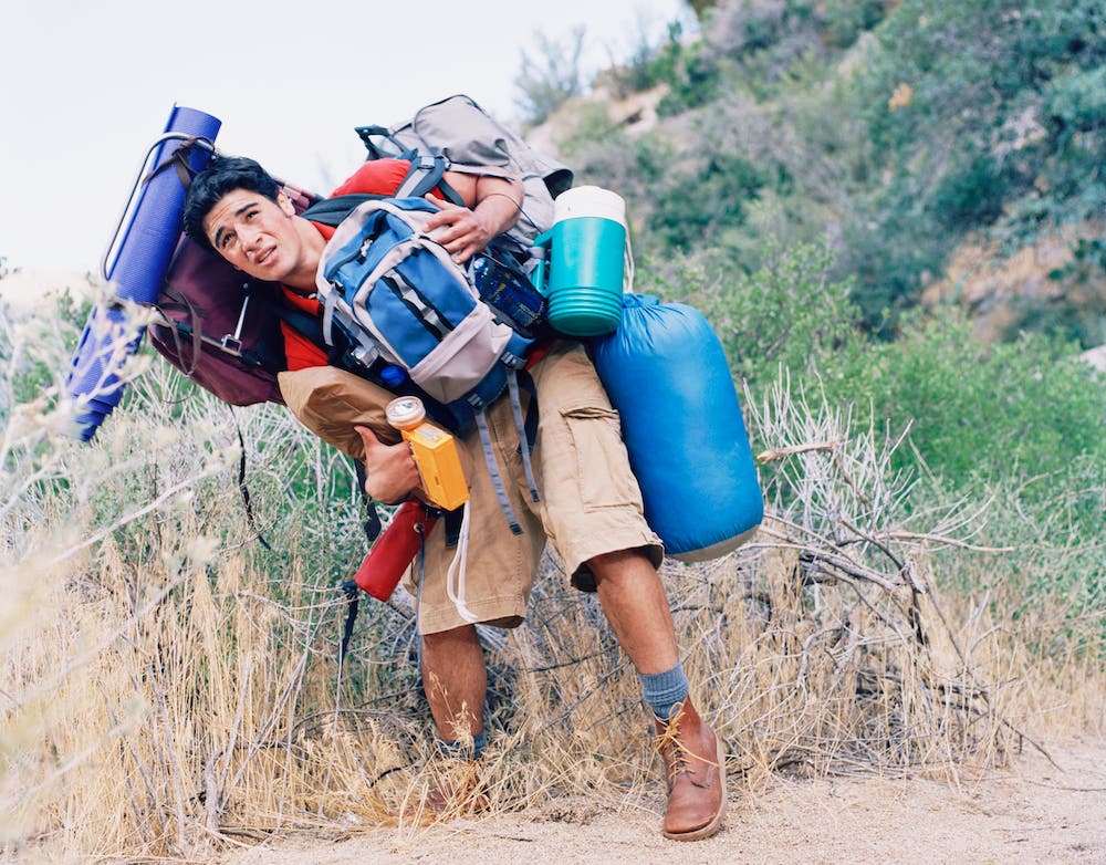 Young man carrying way too much backpack and camping gear outdoors