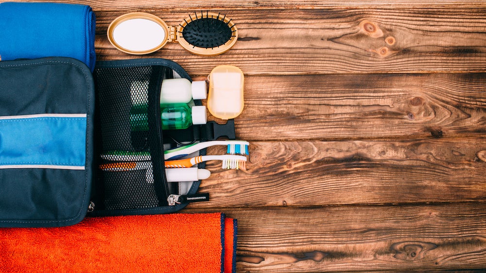 Top view of kit for hygiene during hiking and travel on wooden table with empty space. Items include towel, comb, soap, toothbrushes, shampoo