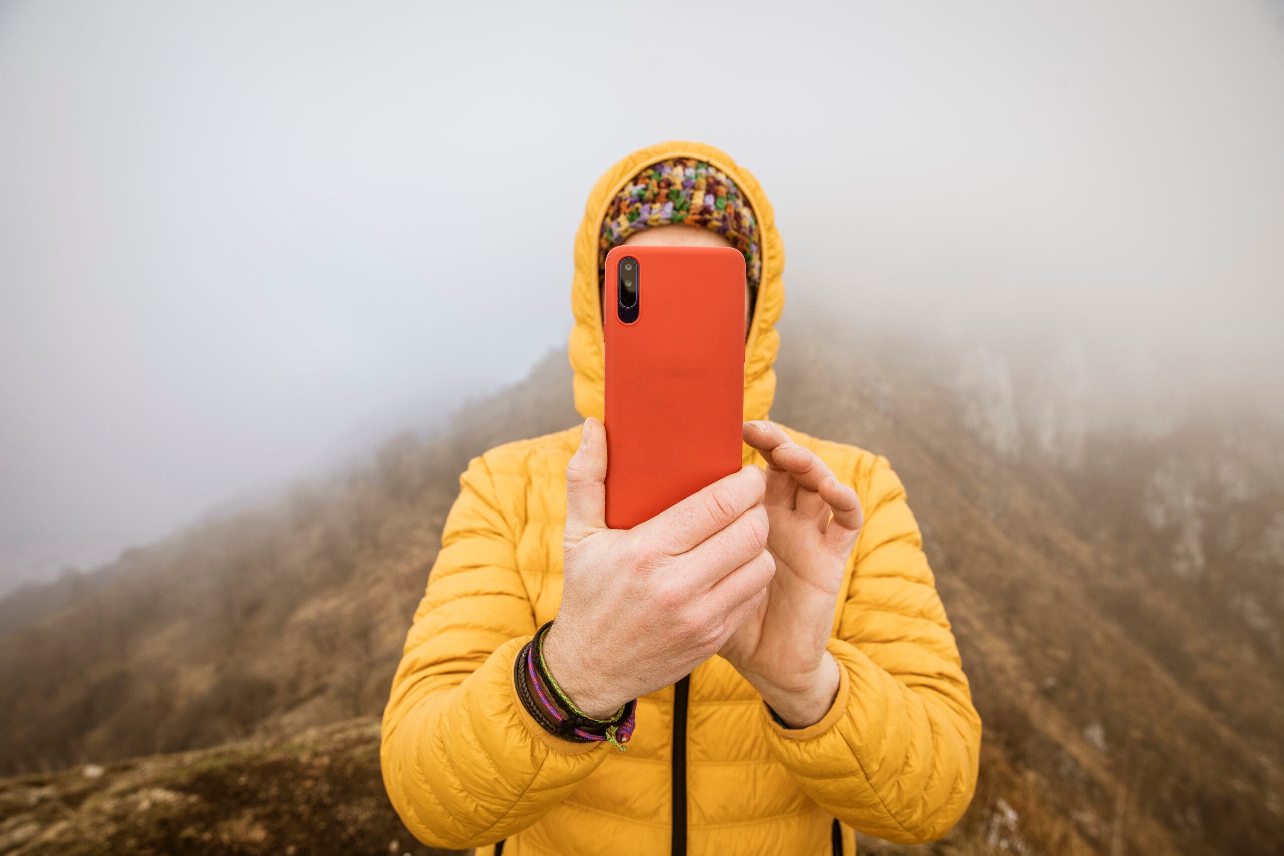 man with yellow hooded down jacket photographing with smartphone
