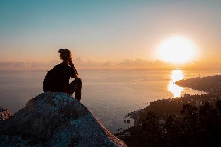 hiker rest on the edge of a high cliff with sunset views of the city and the sea