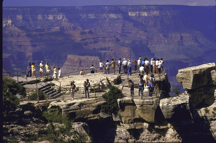 Tourists get breath taking view of Grand Canyon at or near Mather Point with sky bathed in pastel hues of sunrise or sunset.