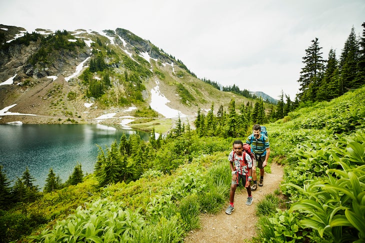 Father and son hiking on mountain trail near alpine lake during backpacking trip