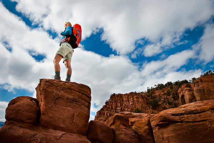 Female hiker standing on rock near red cliffs.