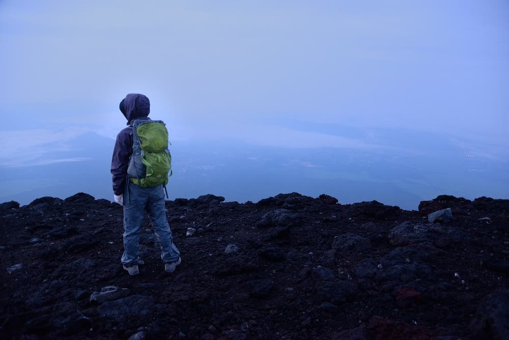 A hiker standing near the crater of Mt. Fuji, watching the sunrise.