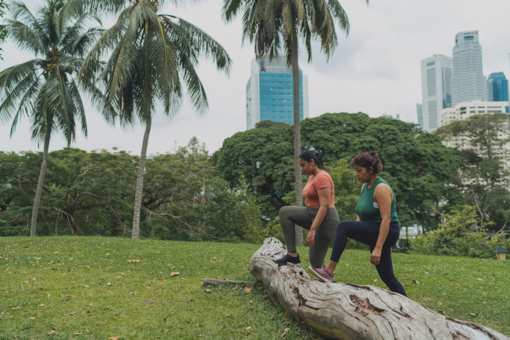 Two women doing step ups on a log in an outdoor park