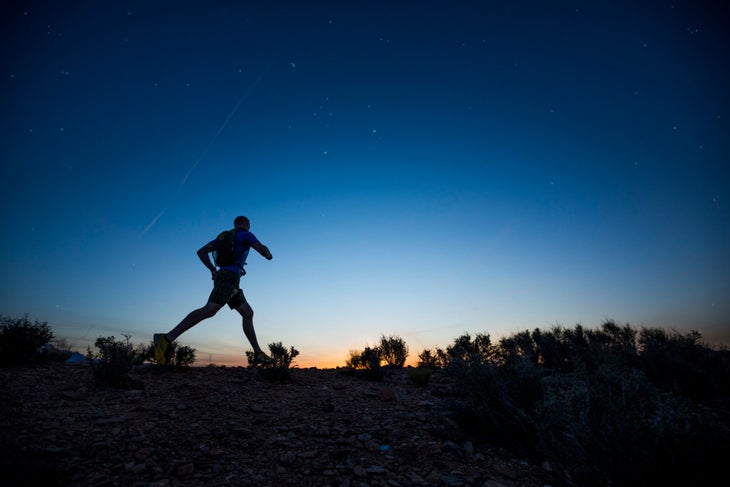 Silhouette of a runner against a dark blue sky. The sun is beginning to brighten the horizon. 